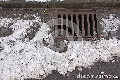 1 - Melting snow flows into an iron kerbside surface drain Stock Photo