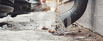 Melting water pouring from steel downpipe fixed on concrete wall Stock Photo