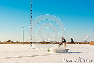 Member of ice skating club dusts off snow of natural ice skating rink in Grootschermer Netherlands Editorial Stock Photo