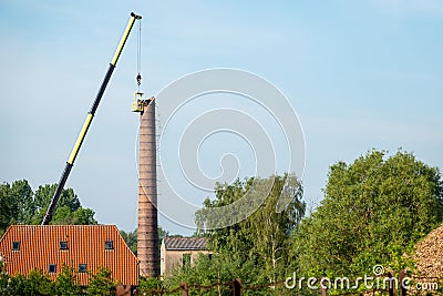 men in a basket hanging from a gigantic crane, painstakingly removing a factory chimney Stock Photo