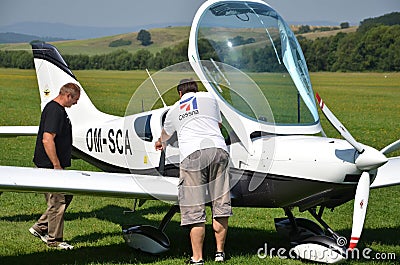 Men check the small personal airplane before taking off and prepare for the flight next to grass landing strip Editorial Stock Photo