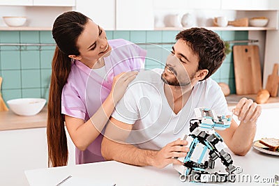 A man collects a robot in the kitchen. The girl gently hugs him from behind. They are smiling. Stock Photo