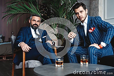 Men with a great style. Two young handsome men in suits looking at camera while resting indoors. Stock Photo