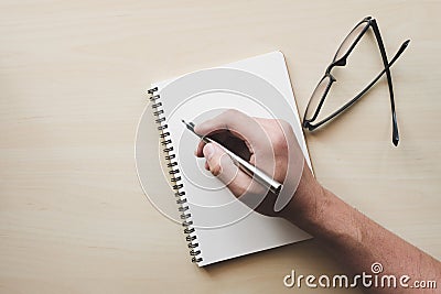 Men hand with pen writing to blank notebook on wooden table close to glasses. Stock Photo