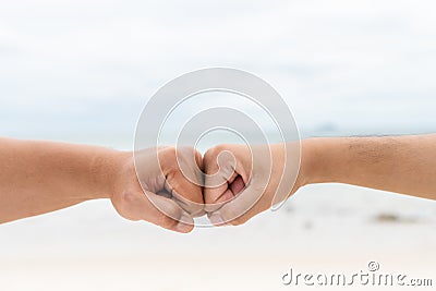 Men hands fist bumping together on blurred sea and sky Stock Photo