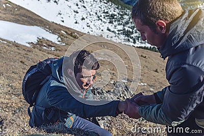 Man helps his friend to climb to the top. Hiker gives a hand to pull up the on mountain. Stock Photo