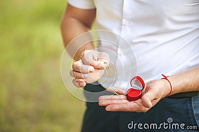 A man makes a proposal to beloved. Male hand holds wedding ring on the background of green nature. Stock Photo