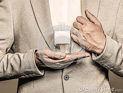 Men perfume in the hand on suit background. Man in formal suit, bottle of perfume, closeup. Fragrance smell. Men Stock Photo