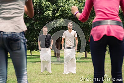 Men playing sack race with girlfriends cheering Stock Photo