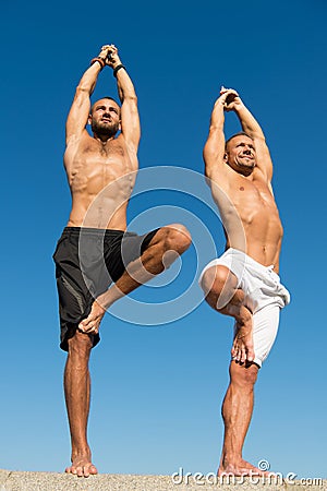 Men practice yoga outdoors. Muscular men training on fresh air. Reach balance by virtue of yoga. Sport and health care Stock Photo