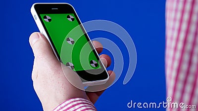 Men`s hand holding the smartphone in a vertical position. Green screen on the phone and blue chromakey. Tracking markers Stock Photo