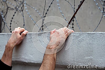 Men`s hands on a concrete fence against a background of barbed wire. Stock Photo