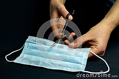 Men`s hands cut through the medical mask, preventing it from being reused or sold. Proper disposal of the used medical mask. Stock Photo