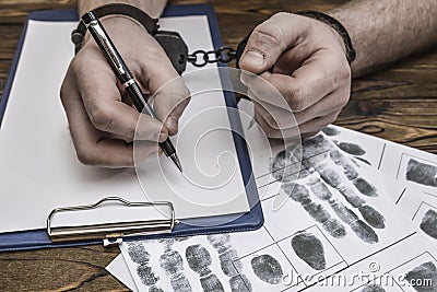 Men`s hands with handcuffs fill the police record, confession. Stock Photo