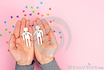 Men`s hands holding a couple of gay men cut out of paper on a pink background. Valentine`s Day, gay pride day. Lgbt concept Stock Photo