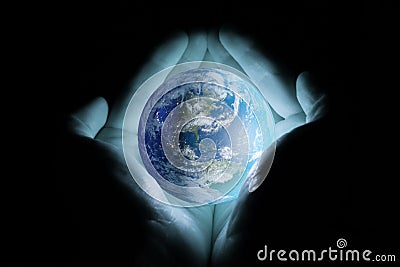 Men`s hands holding the planet earth with a blue glow on a black background. Stock Photo