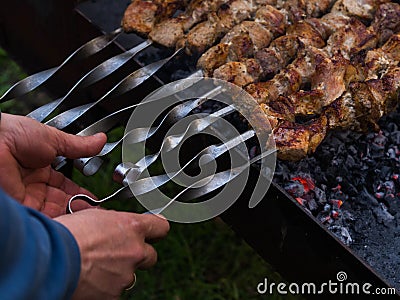 Men`s hands overturn skewers with meat roasted Stock Photo