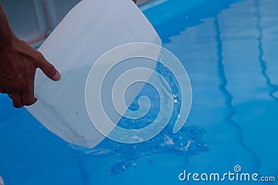 Men`s hands pour light liquid from a plastic tank into a pool, into water. chemical water purification, alkali balance, unsanitar Stock Photo