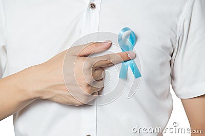 Men`s healthcare concept - close up of male hand pointing to light blue ribbon for prostate cancer at left chest isolated Stock Photo