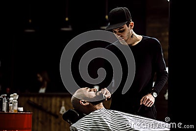 Men`s style. The barber dressed in a black clothes scissors beard of brutal man in the stylish barbershop Stock Photo