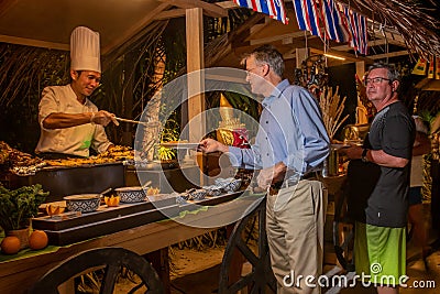 Men selecting food during the international cuisine dinner outdoors setup at the tropical island restaurant Editorial Stock Photo