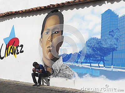 A men sitting on a street in Caracas with ex president Hugo Chavez graffiti in the background Editorial Stock Photo