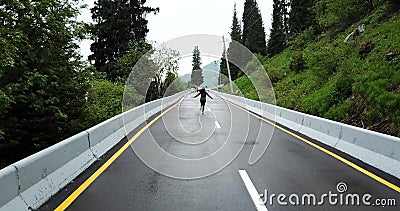 A menina corre no asfalto molhado O terreno montanhoso, os lados da estrada é abeto vermelho e grama verde filme A menina corre no asfalto molhado O terreno montanhoso, os lados da estrada é abeto vermelho e grama verde filme