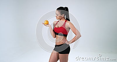A menina nova, desportiva guarda uma laranja em seus mão e sorriso isolada no fundo branco 4K video estoque A menina nova, desportiva guarda uma laranja em seus mão e sorriso isolada no fundo branco 4K video estoque