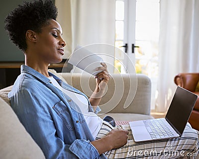 Menopausal Mature Woman At Home With Laptop Having Hot Flush Fanning Herself Stock Photo
