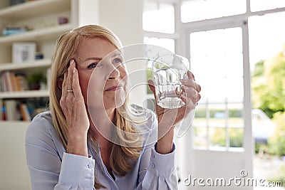 Menopausal Mature Woman At Home Suffering With Headache Pain Drinking Glass Of Water Stock Photo