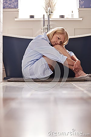 Menopausal Mature Woman Suffering With Incontinence Sitting On Bathroom Floor At Home Stock Photo