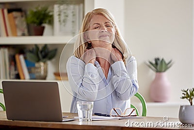 Menopausal Mature Woman Suffering Neck Pain Working On Laptop At Home Stock Photo