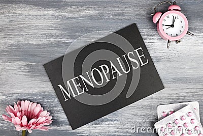 menopause word written on black board, flowers, clock and pills on wooden background. Stock Photo