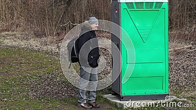 Mens die dichtbij groen draagbaar toilet in het park wachten Mens die dichtbij groen draagbaar toilet in het park wachten