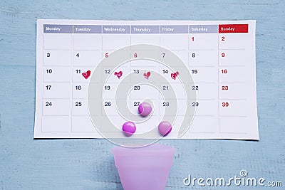 Menstrual calendar with pills and sanitary cup on table Stock Photo