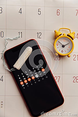 Menstruation app in smartphone with cotton tampon and alarm clock on a calendar. Woman critical days and hygiene Stock Photo