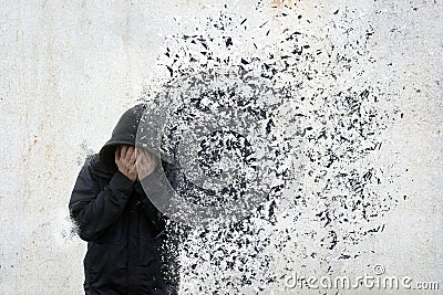 A mental health concept of a hooded man holding his head in his hands. With his body disolving and floating away Stock Photo