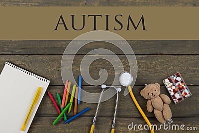 Mental health concept - text Autism, notepad, pills, yellow stethoscope, Teddy bear toy, crayons on wooden background Stock Photo