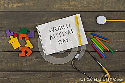 Mental health concept - text World Autism day, notepad, yellow stethoscope, colorful wooden jigsaw puzzles, crayons Stock Photo