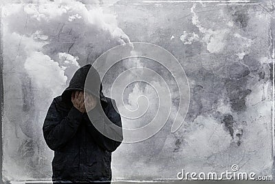 A mental health, emotional concept. Of a hooded man holding his head in his hands, with storm clouds behind. With a painted grunge Stock Photo