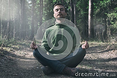 Mental health, mindfulness concept. Young bearded man practicing yoga outdoor, sitting in pose of lotus with eyes closed and Stock Photo