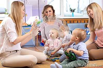 Mentor and 1 years old babies play with educational toys in kindergarten or daycare centre Stock Photo