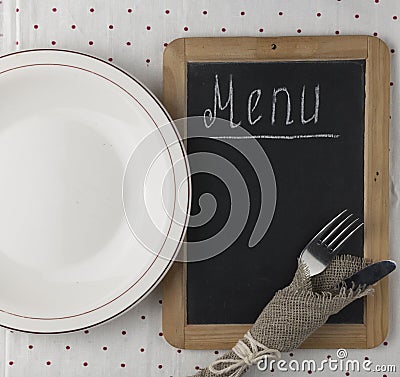 Menu title written white chalk on blackboard with table setting knife and fork lying on tablecloth polka dot. Copy space for your Stock Photo