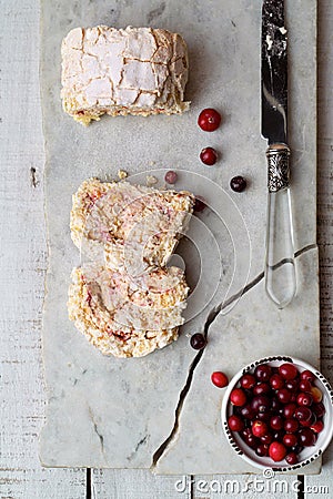 Meringue roll cake, fresh cranberries on creacked marble board, top view Stock Photo