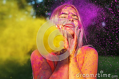 Merry blonde woman posing with exploding yellow paint at summer Stock Photo