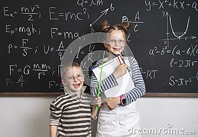 Merry boy and girl pupils are standing at the blackboard and the stetrads. Many formulas are written on the blackboard. Stock Photo