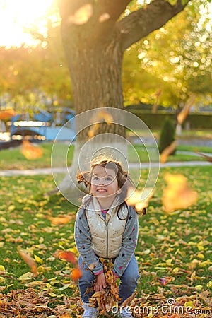 A merry child scatters an armful of yellow fallen leaves. Sunny sunset in autumn park outdoors Stock Photo