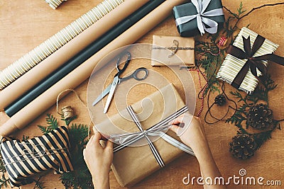 Merry Christmas, flat lay. Hands wrapping stylish christmas gift box in craft paper and scissors, rustic presents, thread, pine Stock Photo