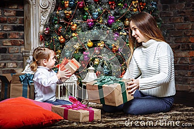 Merry Christmas and Happy Holidays! Cheerful mom and her cute daughter exchanging gifts. Parent and little child having fun near C Stock Photo