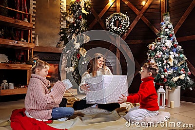 Merry Christmas and Happy New Year. Cheerful mom and her cute daughter and son exchanging gifts. Parent and children Stock Photo